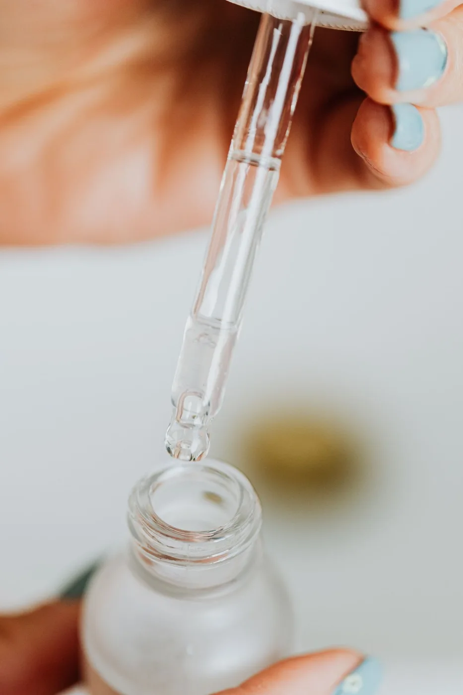 Hands dispensing skincare serum from a glass dropper